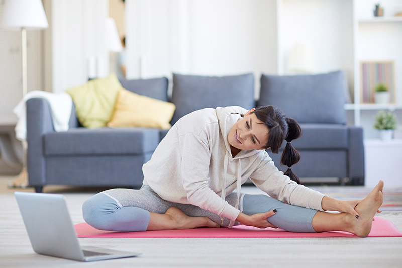 Eine Frau sitzt im Wohnzimmer auf einer Sportmatte und dehnt sich (laute Nachbarn).